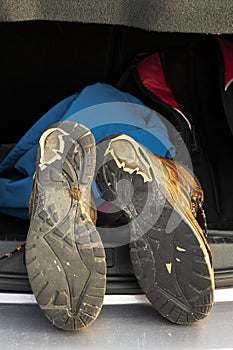 Pair of old brown hiking shoes on a car boot and red backpack. Reliable leather worn out boots. Long walk or travel trip concept.