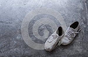 A pair of old dirty shoes on the cement floor with light shading from the corner.
