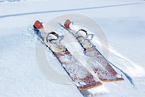 Pair of old fashioned wooden brown skis on white snow. Vintage winter background