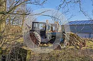 A Pair of Old unused Tractors, parked up in light Woodland next to a Modern barn at a Farm at the Mains of Arbilot.