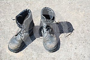 Pair of old used work boots on concrete background. Dirty black leather boots from the army