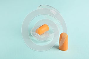 Pair of orange ear plugs and case on turquoise background