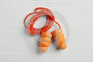 Pair of orange ear plugs with cord on white wooden background  top view
