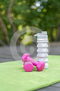 Pair of pink dumbbells and silicone water bottle on yoga mat. Fitness and activity outdoors. Sport and healthy lifestyle concept.