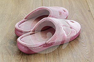 Pair of pink female house slippers on a brown wooden floor. Cozy, warm and comfortable domestic shoes