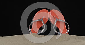 Pair of pink flip flops embellished with rhinestones stick out of the sand. Slider shot. Isolated