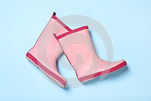 Pair of pink rubber boots on light blue background, top view