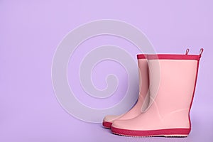Pair of pink rubber boots on violet background. Space for text