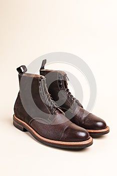 Pair of Premium Dark Brown Grain Brogue Derby Boots Made of Calf Leather with Rubber Sole Placed Over Beige Background