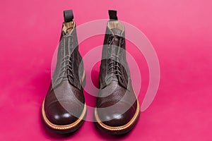 Pair of Premium Dark Brown Grain Brogue Derby Boots Made of Calf Leather with Rubber Sole Placed Over Pink Background