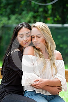 A pair of proud lesbian in outdoors, brunette woman is hugging a blonde woman, in a garden background photo