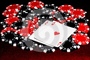 A pair of red aces, diamonds and hearts, on a pile or red and black clay poker chips all on dark red felt surface..  Room for copy