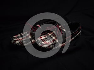 A pair of red black white flat shoes with square pattern taken in the low light with dark background photo