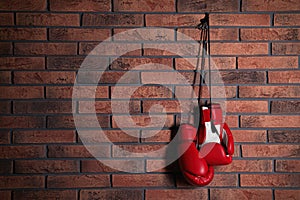 Pair of red boxing gloves hanging on brick wall, space for text