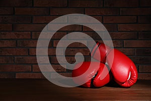 Pair of red boxing gloves on wooden table near brick wall