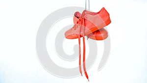 Pair of red female sneakers hanging on white background. Bright coral woman's trainers hang out on the rope