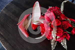 A pair of red high-heeled shoes with a bouquet on the table