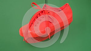 Pair of red sneakers hanging on green background. Orange boots hang out on the rope