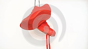 Pair of red sneakers hanging on white background. Orange boots spinning on the rope