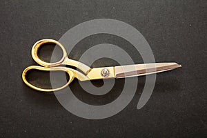 Pair of scissors gold handle on black background, top view