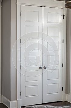 A pair or set of two white painted hall entry closet closed five panel doors in a new construction house with greige