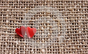 a pair of sharp pins in the form of red hearts stuck in the rough burlap