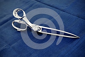 Pair of sharp tailors scissors on blue fabric