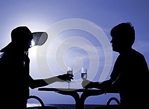 Pair silhouette sit at a table and hold goblets