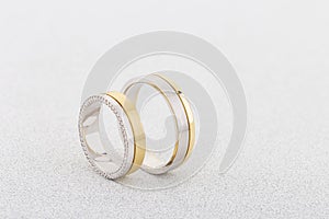 Pair of silver and gold combined rings with diamonds on white glitter background