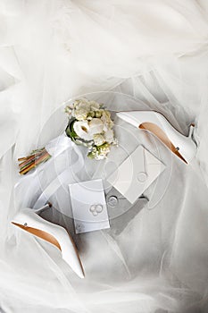 a pair of wedding shoes , a bouquet of flowers , a wedding invitation , and a pair of wedding rings