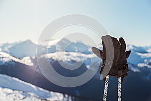 A pair of ski gloves on poles with snowy mountain peaks in the background on a sunny day.