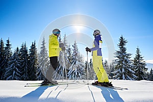Pair of skiers standing on skis one against each other and watching on sun shine in blue sky. Winter recreation concept.