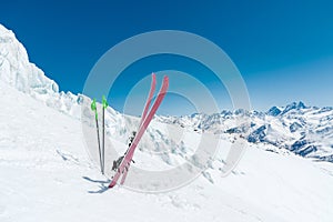 A pair of skis and ski poles stick out in the snow on the mountain slope of the Caucasus against the backdrop of the