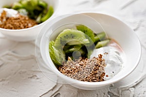 A pair of small dessert bowls with fresh kiwi fruit, white ice cream, yogurt and chocolate chips on a white stone background