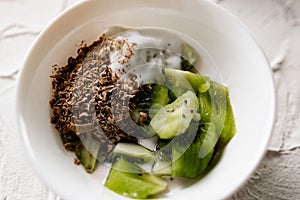 A pair of small dessert bowls with fresh kiwi fruit, white ice cream, yogurt and chocolate chips on a white stone background