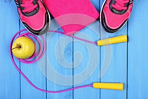 Pair of sport shoes, fresh apple and accessories for fitness on blue boards, copy space for text