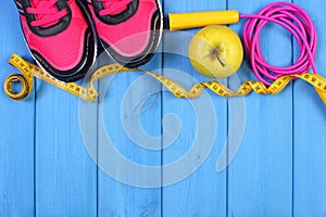 Pair of sport shoes, fresh apple and accessories for fitness on blue boards, copy space for text