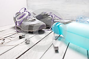 Pair of sport shoes, water bottle and earphones on white wood