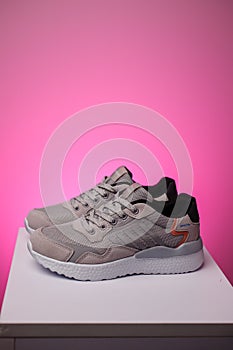 Pair of sports shoes standing on white podium on pink background.