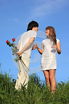 Pair stands, guy holds behind back bouquet