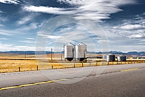 Pair of steel grain silos next to a divided highway along harvested fields