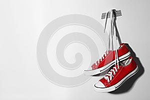 Pair of stylish shoes with laces hanging on white wall, space for text