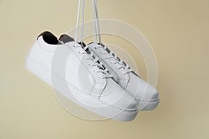 Pair of stylish sports shoes hanging on beige background