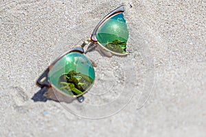 Pair Of Sunglasses On The Beach With A Reflection Of A Beautiful