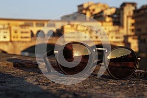 A pair of sunglasses reflects the setting sun with the famous Ponte Vecchio in Florence