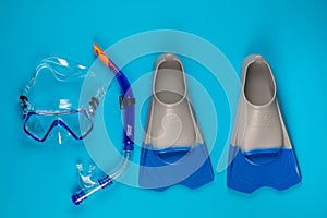 A pair of swimming goggles next to a pair of fins, on blue background