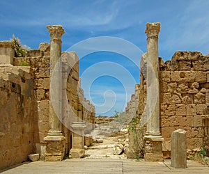 A pair of tall columns against stone walls under a blue sky at ancient Roman ruins of Leptis Magna in Libya