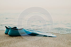 Pair of teal flippers on sandy sea or ocean beach, side view. Swimming equipment - fins on shore. Summer vacation, fun photo