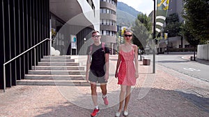 Pair of tourists are walking in small city, chatting and looking landmarks, man and woman are strolling