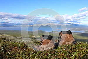 A pair of trekking boots on the edge, other mountains and lake i